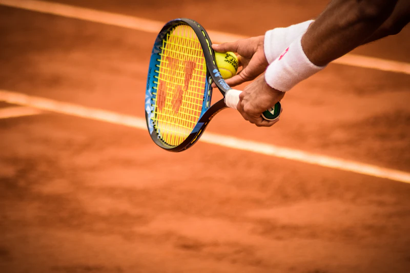 Hands of a player holding a racket and a ball over a clay court.